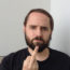 Picture of a white male in a black shirt holding his middle finger up to the camera