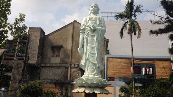 Photo of a large, light green Buddha standing on a lotus flower surrounded by palm trees.