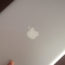 Image contains a grey MacBook Pro being held at an angle by a hand against a brown background.