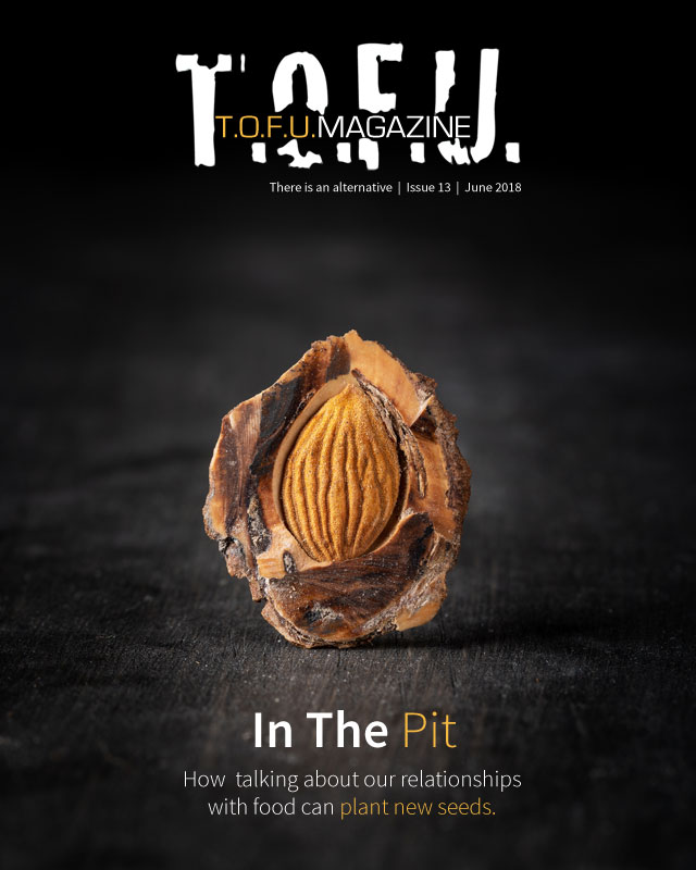 Image contains a dark background with a peach pt in the middle. The pit has been cut open to show the light brown seed. Above the pit, there is text that says "T.O.F.U." in white, and within that text there is more text that says "T.O.F.U. Magazine". Just below the white T.O.F.U., there is text that says "There is an alternative | Issue 13 | June 2018". Below the pit, there is more text that says "In the pit. How talking about our relationships with food can plant new seeds."