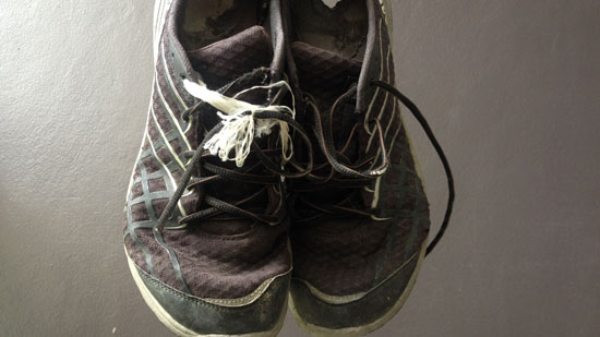 Image contains a pair of old black fabric shoes with white stripes against a grey background.