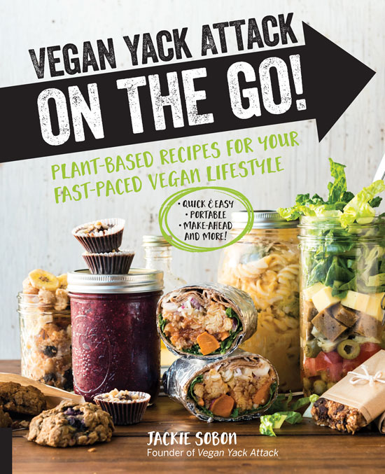 Image contains a grey background with black text at the top that says "Vegan Yack Attack" and a black arrow below that spans the width of the whole image. Within this arrow, white text says "On the Go!". Below the arrow, there is green text that says "Plant-Based Recipes For Your Fast-Paced Vegan Lifestyle". Below the text, in the remaining half of the image, there are a series of jars with food items such as pasta, a smoothie, salad, and more. As well, salad wraps and cookies are included on a wooden countertop.