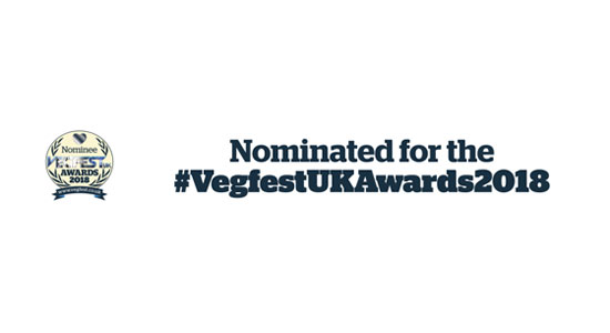 Image contains a white background with a circular logo in the centre-left. Within the logo is a heart on the top and the words "Nominee Vegfest UK Awards 2018" below. On either side of the text, there are two sets of leaves. Below the circle, there is a small banner that says "www.vegfest.co.uk". To the right of the logo, there is black text that says "Nominated for the" on one line and "#VegfestUKAwards2018" on another.