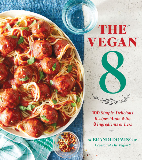 Image contains two columns with the left column containing a blue tablecloth and a light green napkin. On the tablecloth, a white plate is filled with spaghetti and meatballs. Just below the plate, there is a small dish of crushed chili peppers. In the right-hand column, there is text on a white stone background that says "The Vegan 8" above a small illustration of leaves. Below this illustration, there is text that says "100 simple, delicious recipes made with 8 ingredients or less" and then a series of small dots in a single line. Below these dots, there is text that says "Brandi Doming Creator of The Vegan 8".