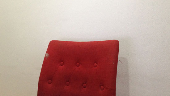 Image contains a photo of a red fabric chair against a white wall.