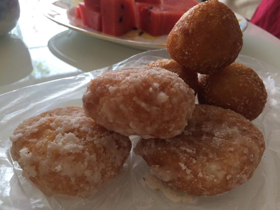 Image contains a photo of Vietnamese banh cam along with a sugared variety. In the background, lives of watermelon are visible.