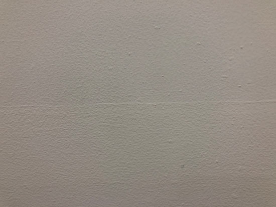 Image contains a photo of a painted white wall with small bumps and a thin line going across the middle.